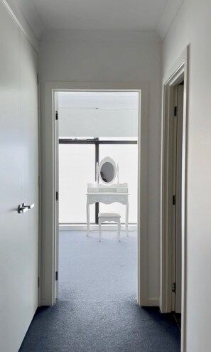 A hallway leading to a room with a white vanity and a large mirror.