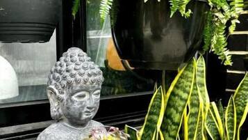 A statue of a seated figure holding a fish bowl, surrounded by plants and a window.