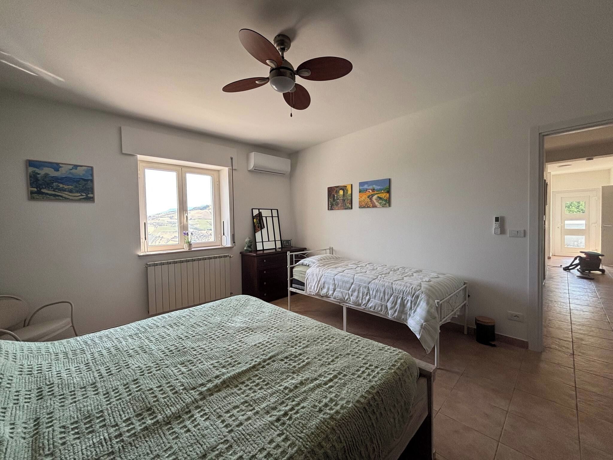 Un dormitorio con dos camas, un ventilador de techo, una ventana con vistas y obras de arte en las paredes.