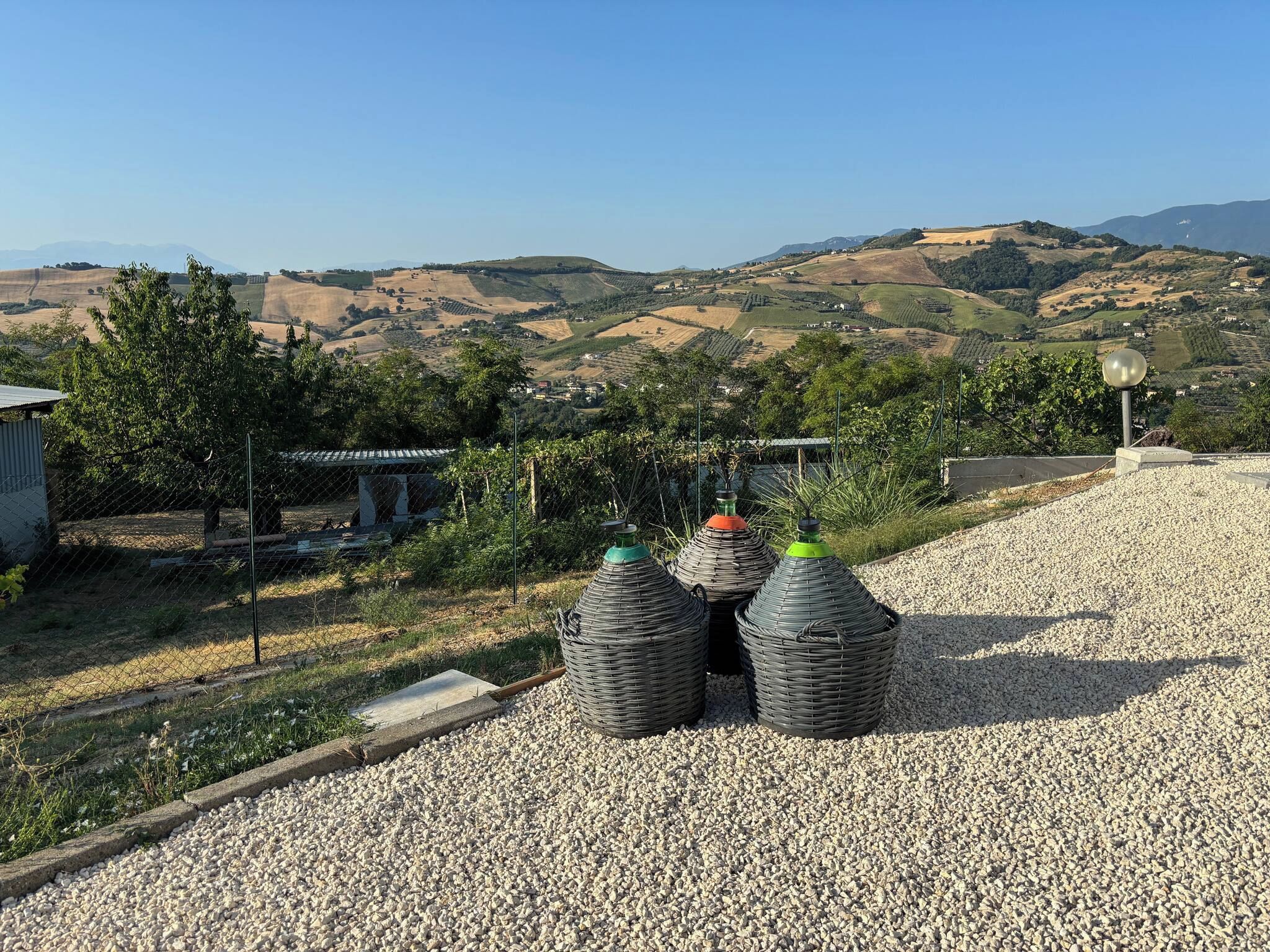 A gravel area with four large, woven containers, a fence, and a clear view of rolling hills and distant mountains.