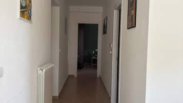 Een gang met een radiator, een plafondlamp en kunstwerken in lijsten aan de muur.