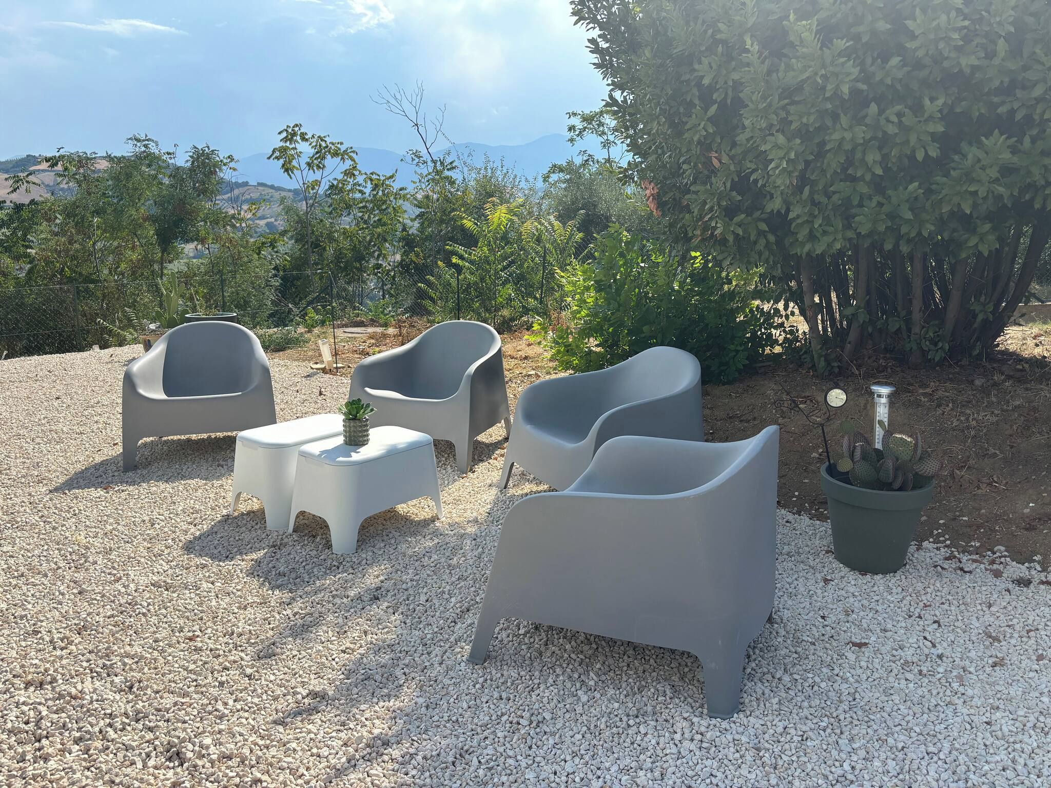 An outdoor seating area with modern chairs and a small table, surrounded by gravel and greenery.
