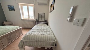 Une chambre avec un lit simple, un radiateur, une fenêtre et un petit tabouret.