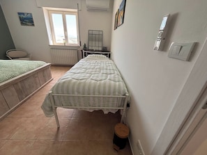 Un dormitorio con una cama individual, un radiador, una ventana y un taburete pequeño.