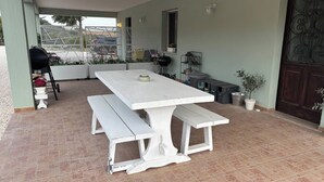 Une terrasse avec une table et un banc blancs, un barbecue et des plantes en pot.