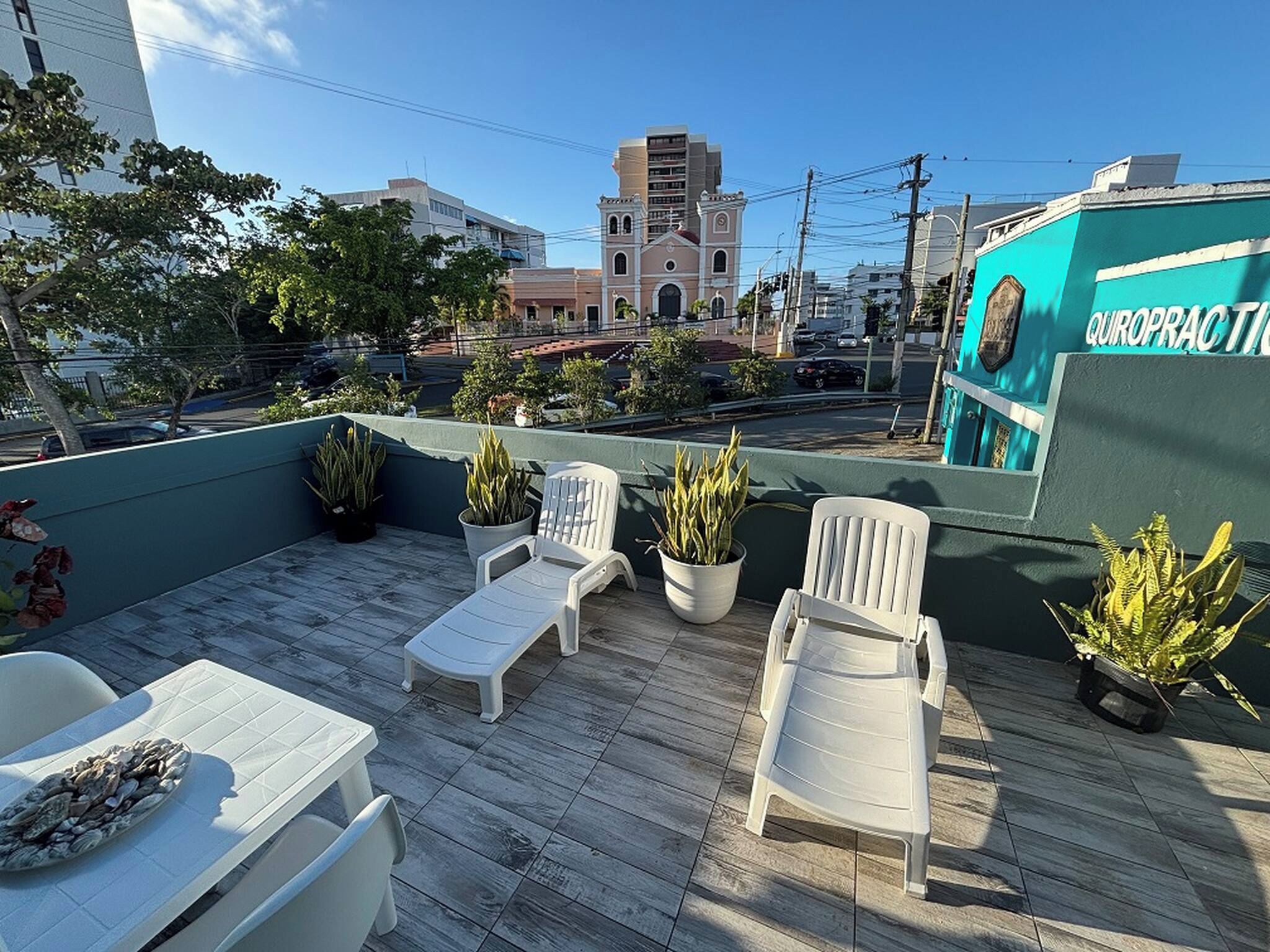 Una terrazza sul tetto con poltrone da relax bianche, piante in vaso e vista sulla città.