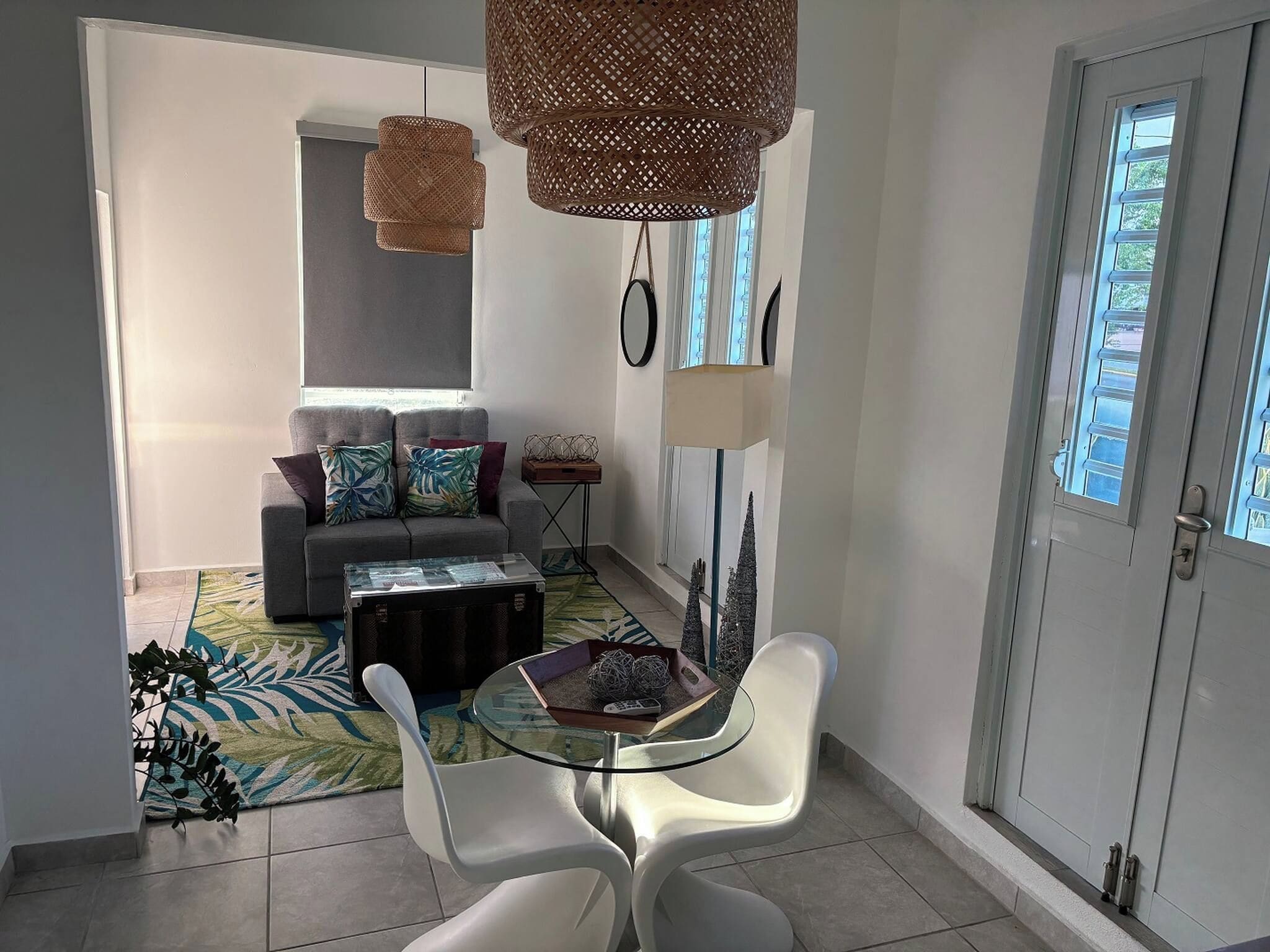 A modern living room with a sofa, a glass coffee table, and a dining area with white chairs.
