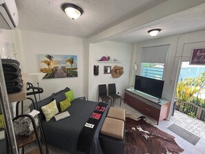A hotel room with a bed, a TV, a desk, and a window with a view of the outside. - Tiny Cozy Studio 15 minutes Airport, Patio, small share pool one full bed (San Juan city)