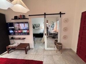 Ein Wohnzimmer mit Fernseher, Couchtisch, rotem Teppich und einer Schiebetür, die in einen Essbereich führt.