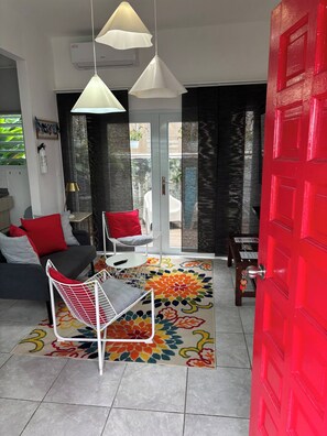 Ein modernes Wohnzimmer mit einer Couch, einem Sessel, einem farbenfrohen Teppich und einer roten Tür.