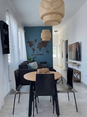 Ein modernes Wohnzimmer mit einem runden Holzesstisch, schwarzen Stühlen, einer Wandmalerei einer Weltkarte, einer gewebten Leuchte und einem Fernseher an der Wand.