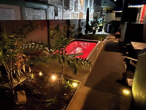 Ein Außenbereich bei Nacht mit einem roten Pool, Topfpflanzen und einem Weg.