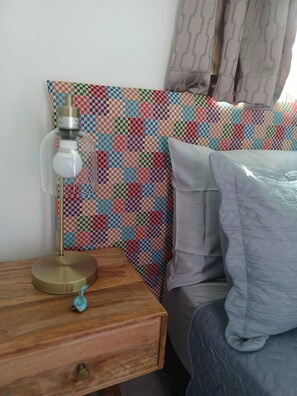 Ein Bett mit einer gesteppten Kopfteil, ein Nachttischchen mit einer Lampe und eine Schublade.