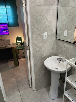 A bathroom with a white sink, a mirror, and a green chair. - Apartment, 2B, AC, pool 10 minutes Airport (San Juan city)