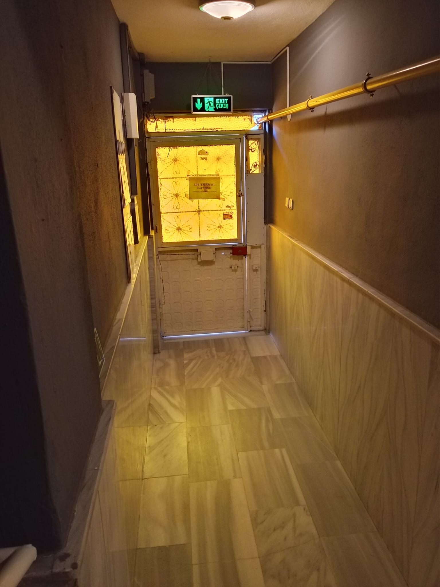 Un pasillo con piso de madera, una puerta con un letrero y una lámpara en el techo.