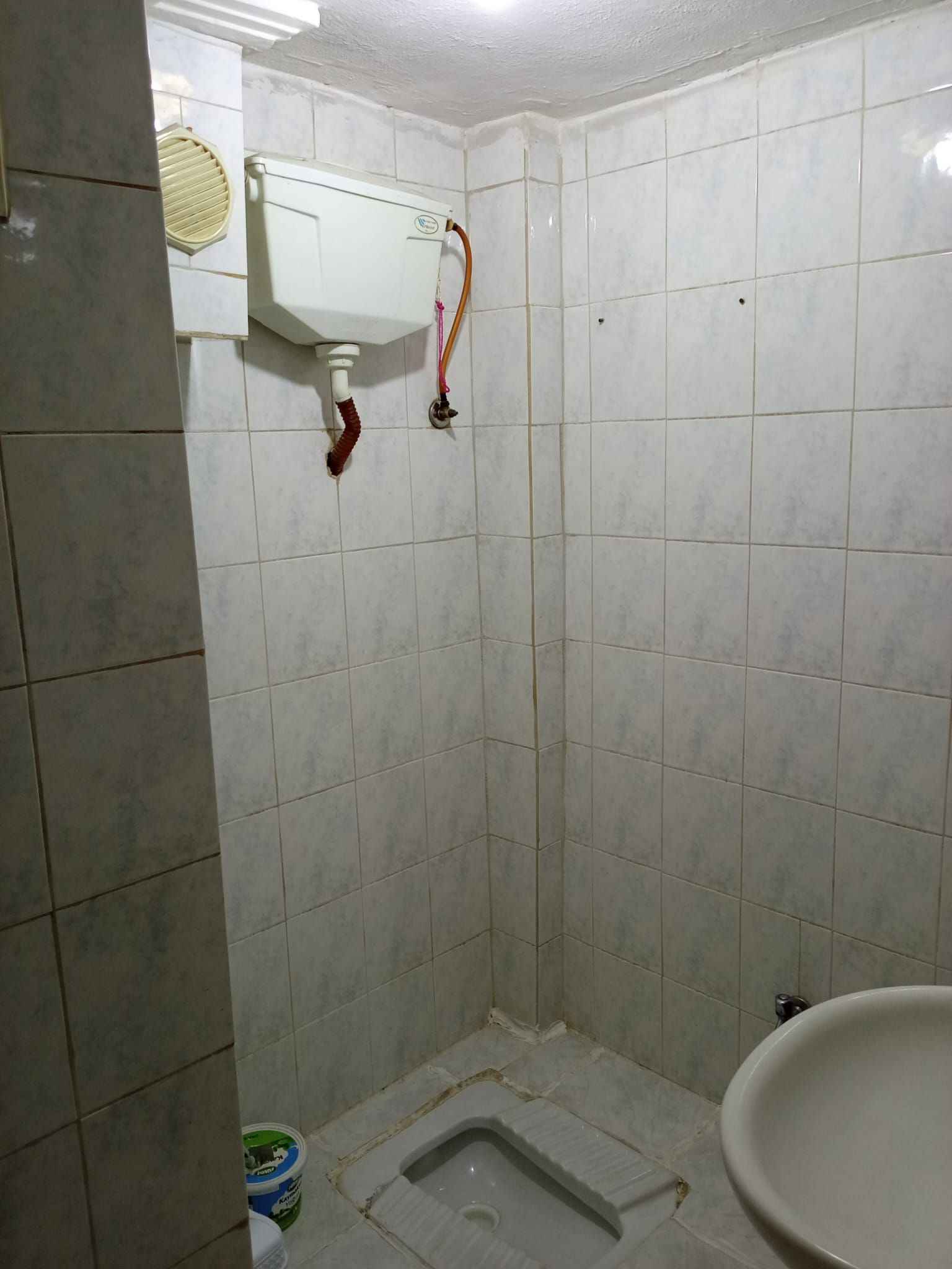Un baño con azulejos blancos, inodoro, lavamanos y zona de ducha.