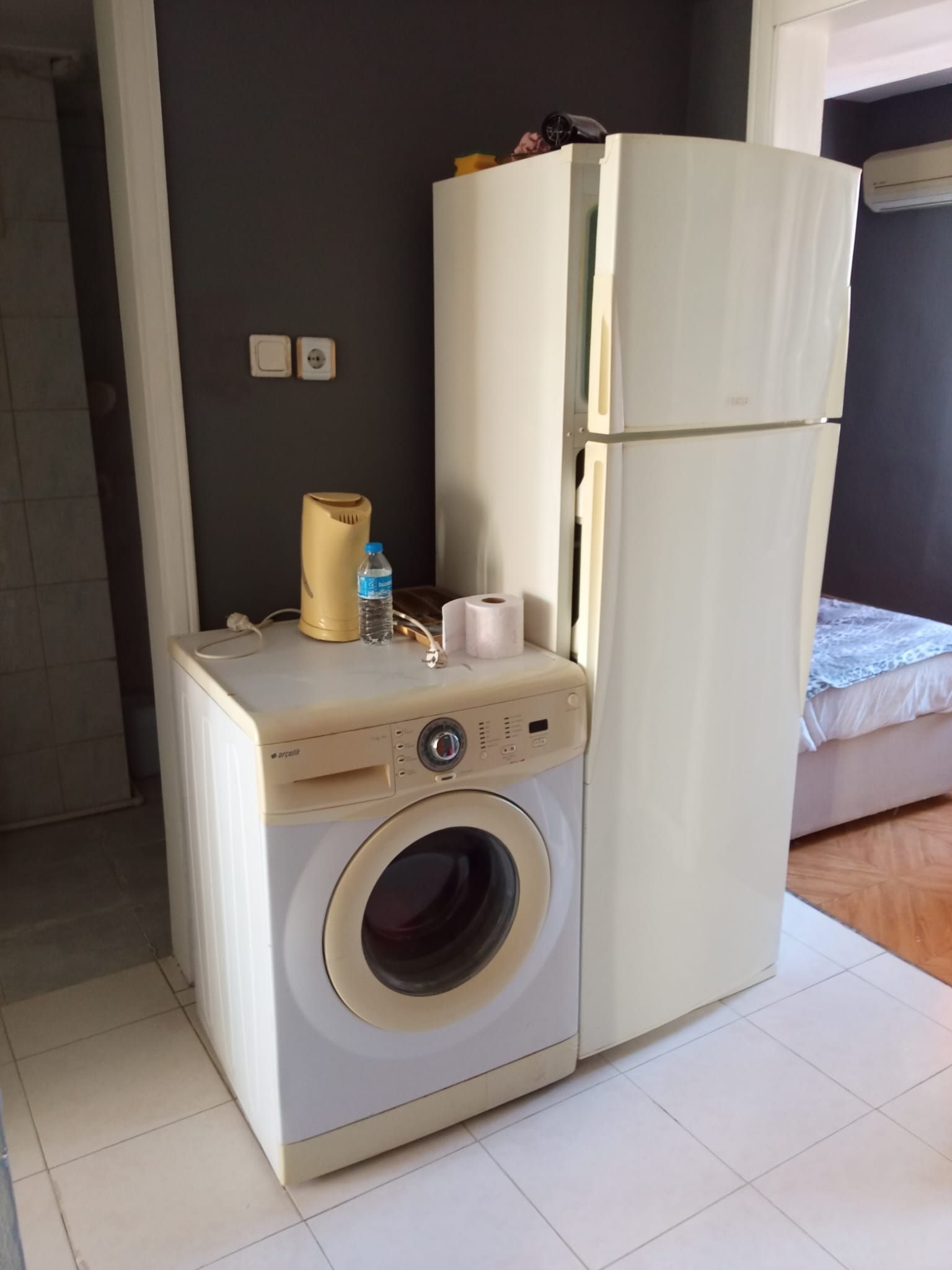 Una habitación compacta con lavadora, un calentador pequeño y un refrigerador.