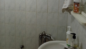 Een badkamer met een wit wastafelmeubel, een spiegel, een handdoek aan de muur en een zeepfles.