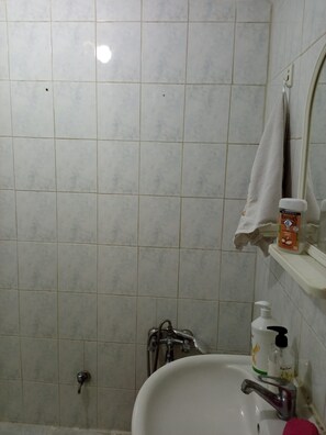 Un baño con un lavamanos blanco, un espejo, una toalla colgada en la pared y una botella de jabón.