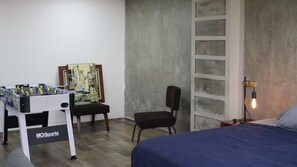 A room with a foosball table, a framed picture, a chair, a bed, and a wall with a light fixture. - Modern Loft King Bed, Wifi & Smart Lock (Mexico City)