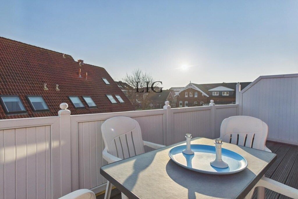 A balcony with a table and chairs, a clear sky, and buildings in the background.
