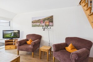 A living room with two armchairs, a small wooden table, a television, and a painting on the wall. - Holiday apartment Uhlenkamp 7 (Langeoog)