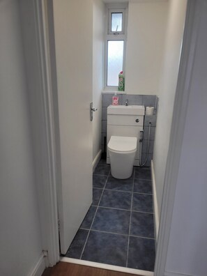 Ein schmales Badezimmer mit Toilette, Waschbecken und einem Fenster über dem Waschbecken.