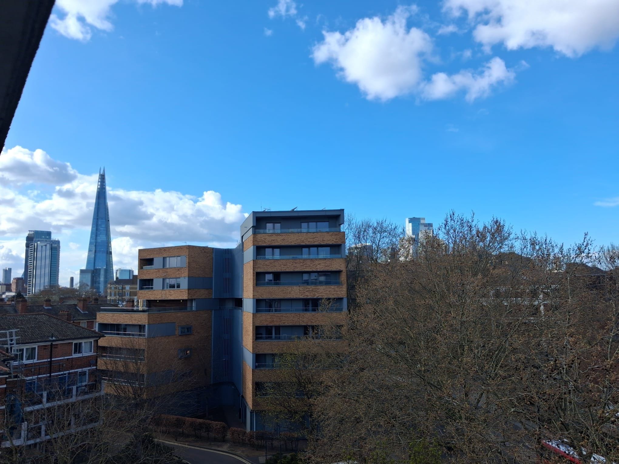Un immeuble à plusieurs étages, doté d’une façade en briques et de grandes fenêtres, entouré d’arbres et d’autres bâtiments.