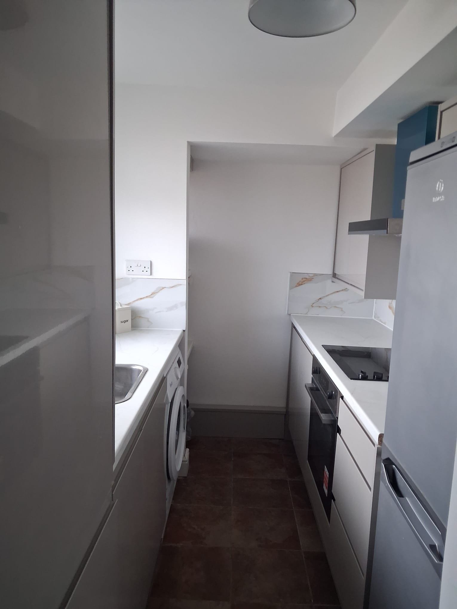 Une cuisine de taille réduite équipée d’un lave-linge, d’un évier et d’un réfrigérateur.