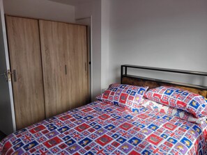Ein Schlafzimmer mit einem Holzschrank, einem Metallbettgestell und einem Bett mit einer gemusterten Bettdecke.