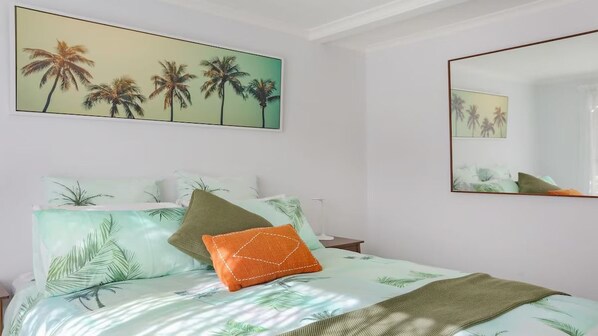 Ein Schlafzimmer mit einem Bett, Kissen, einem Spiegel und einem Palmenbaum-Gemälde.