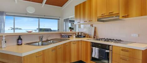 Cocina moderna con armarios de madera, estufa a gas, pileta y vista al mar a través de amplias ventanas.