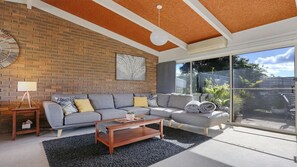 Ein modernes Wohnzimmer mit einer Eckcouch, einem Couchtisch und einem großen Fenster mit Blick ins Freie.