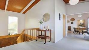 Un interno moderno con una scala in legno, un'area pranzo con tavolo e sedie, e uno specchio rotondo fissato alla parete.