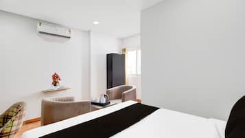 A hotel room with a bed, a chair, a small table with a tray, an air conditioning unit, and a window with curtains.