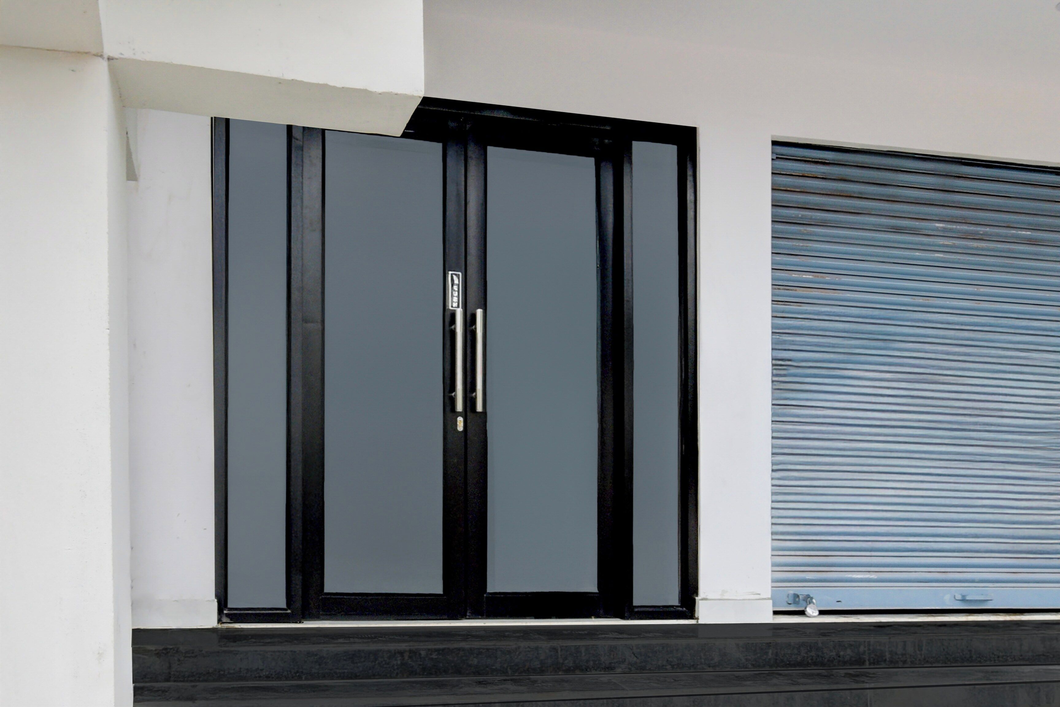 A modern building facade with a black-framed door and a blue roller shutter.