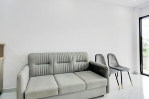 Una sala de estar moderna con un sofá gris, dos sillones estampados y un ventanal grande.