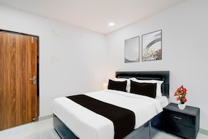 Un dormitorio con una cama, una mesita de noche, un florero con flores y dos cuadros en la pared.