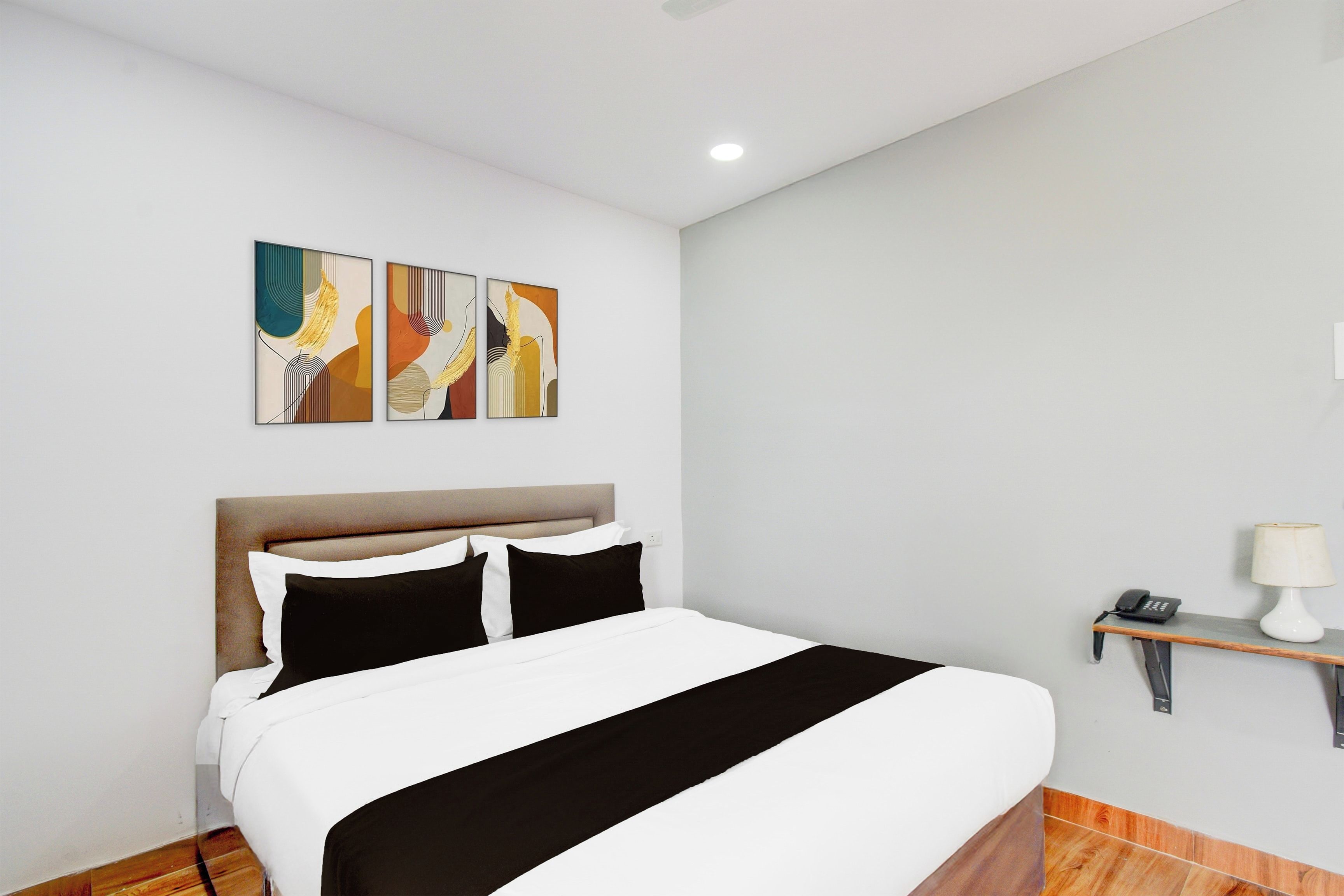 A hotel room with a bed, a headboard, a nightstand with a lamp, and three abstract paintings on the wall.