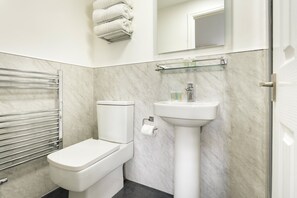 A bathroom with a toilet, a sink, a towel rack, and a glass shelf. - Family Room Near Windermere (Ambleside)