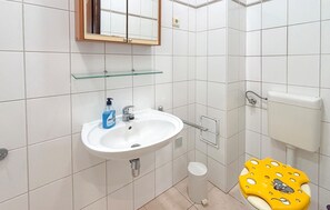 Ein Badezimmer mit einem weißen Waschbecken, einer Glasablage darüber, einer Toilette und einer kleinen Mülltonne.