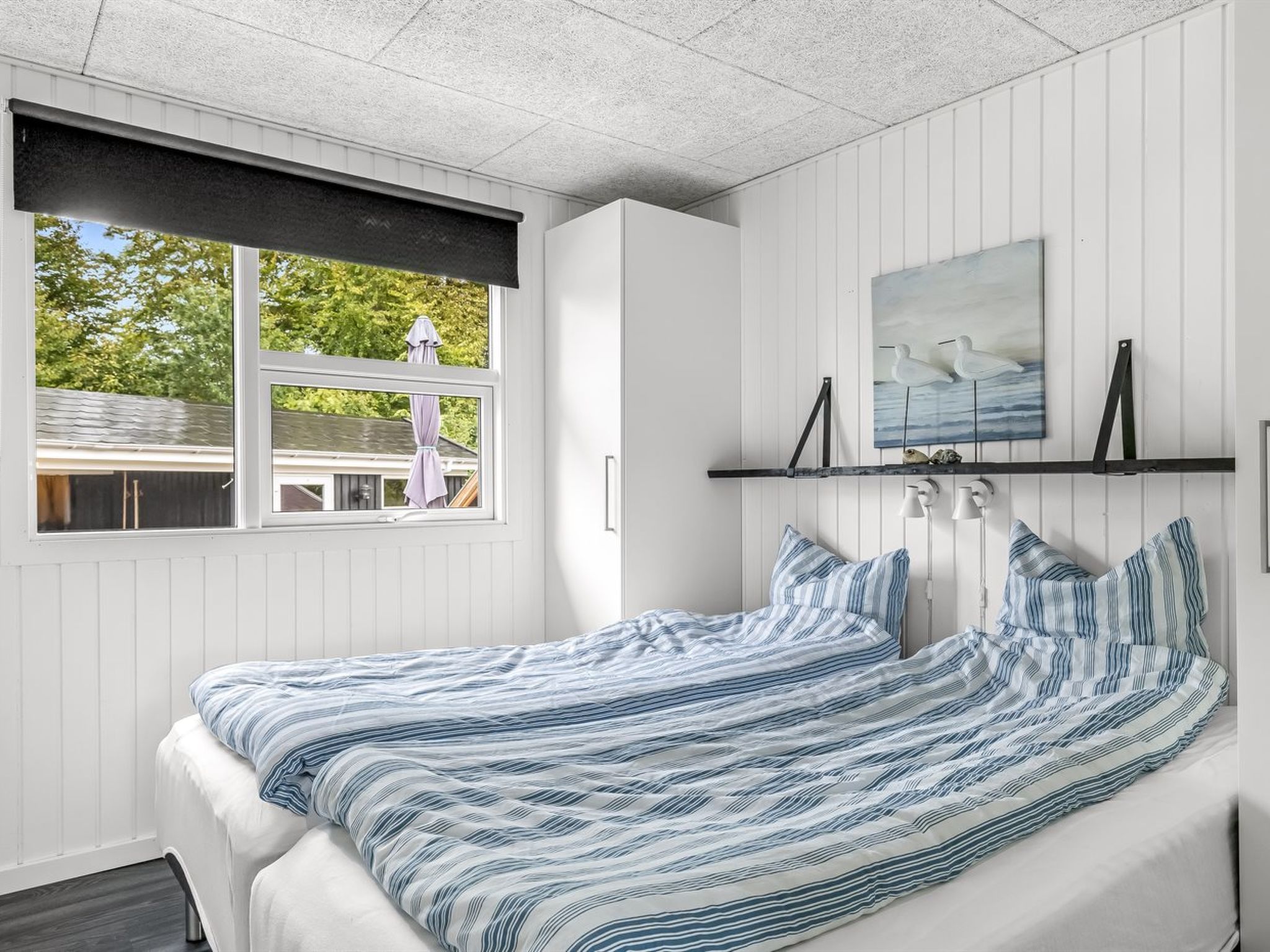 Een slaapkamer met een bed, een raam en een wandplank met decoratieve objecten.
