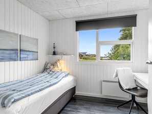 Ein Schlafzimmer mit Bett, Schreibtisch, Stuhl, einem Fenster mit Blick und Bildern an der Wand.