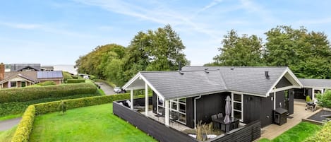 A modern house with a large deck, surrounded by well-maintained lawns and hedges.