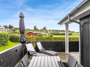 En träaltan med två solstolar och ett bord, ett parasoll och utsikt över en golfbana och hus i fjärran.