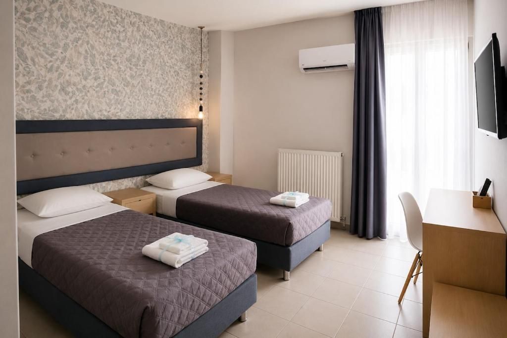 A hotel room with two beds, a desk, a chair, an air conditioning unit, and a television.