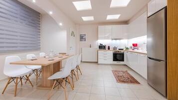 Cocina moderna con comedor, que incluye una mesa y sillas de madera, armarios blancos y un refrigerador de acero inoxidable.