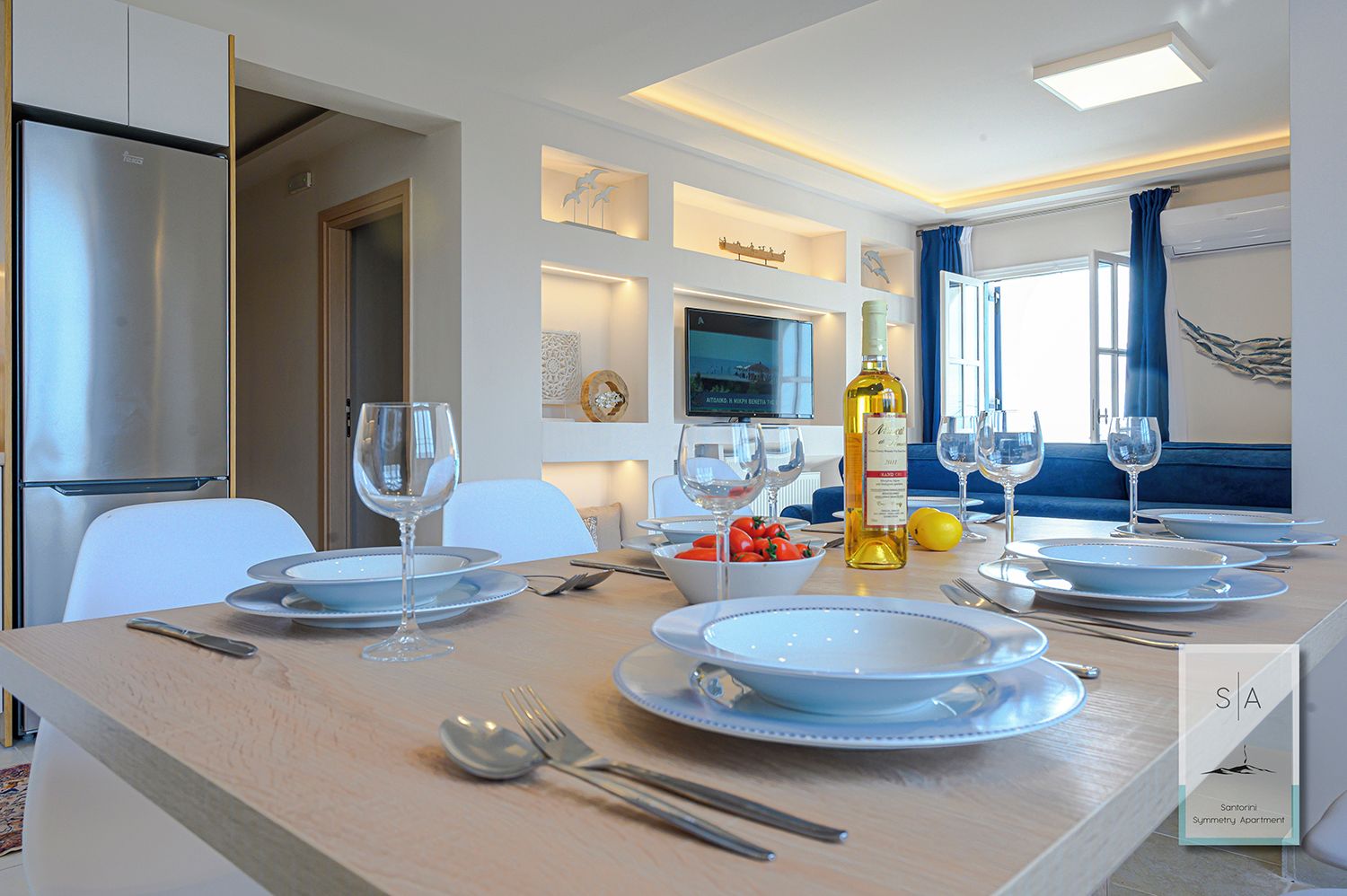A dining area with a table set for two, a bottle of wine, and a bowl of fruit.