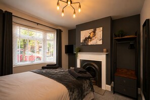 A bedroom with a bed, a fireplace, a TV, and a window with blinds. - Modern 3-Bed, 2-Bath Home | Parking for 3 | Air Conditioning | Rugby (Rugby)