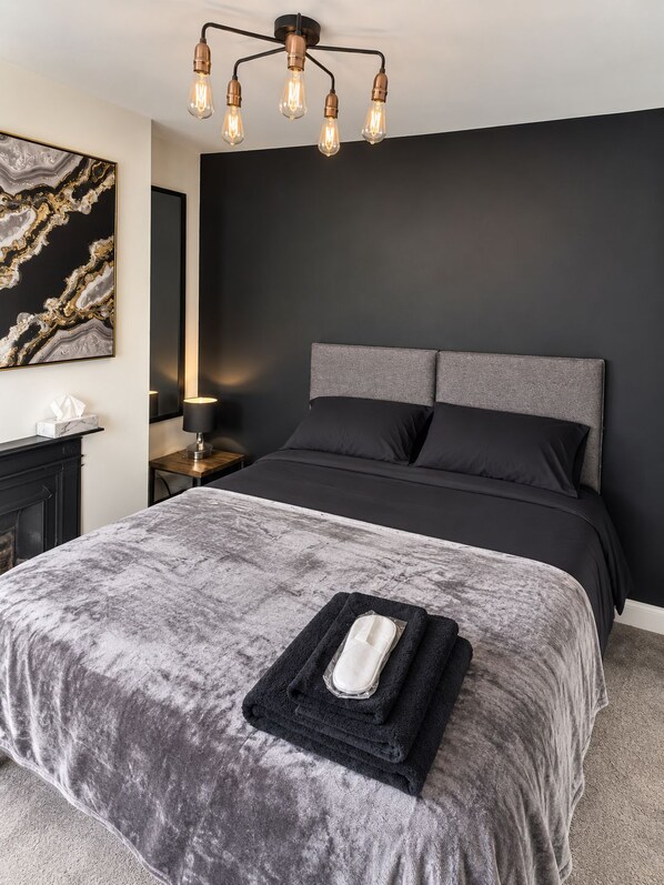 A modern bedroom with a large bed, a headboard, a bedside table, a lamp, and a wall-mounted light fixture.